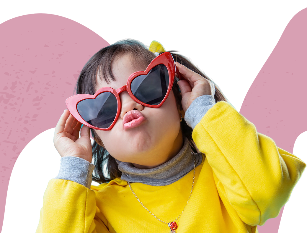 Little girl with big red heart shaped sunglasses pouting for camera with pink squiggle in background.